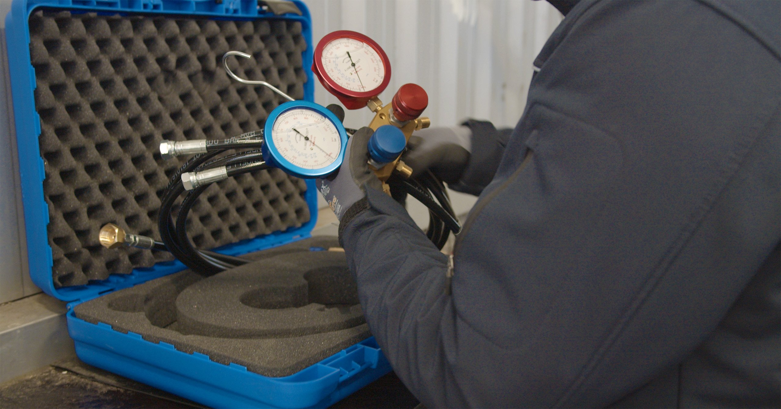Techniker mit Schutzhandschuhen hält ein Manometer-Set zur Kältemitteldruckmessung